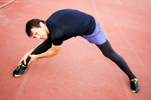 Man is exercising and stretching his legs in stadium outdoors.