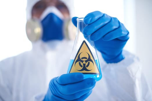 Close-up of flask with blue biohazard liquid in scientist gloved hands