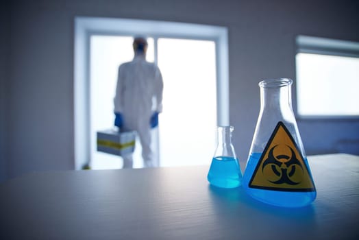 Close-up of two flasks with blue biohazard liquid with scientist on background
