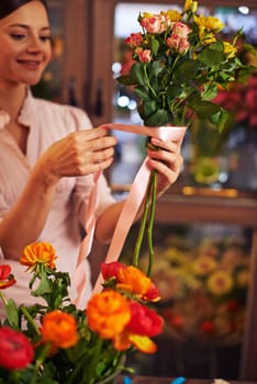 Young woman banding rose bouquet with a ribbon