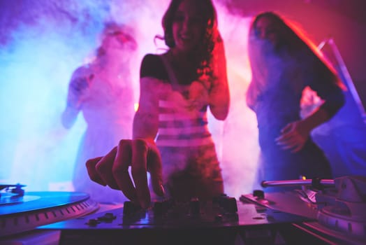 Girl adjusting deejay equipment with her friends behind