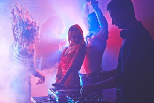 Male deejay mixing sounds with energetic girls and guy dancing on background