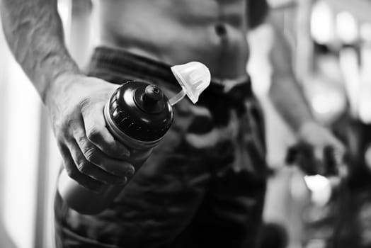 Hand of sportsman holding open plastic bottle with water in gym