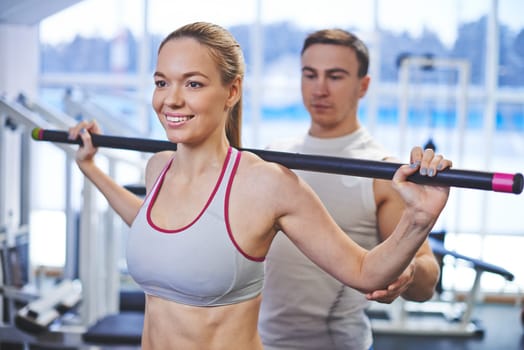 Portrait of pretty girl weightlifting in gym, her trainer helping her