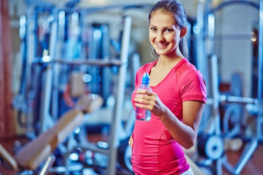 Happy and fit girl with bottle of water looking at camera