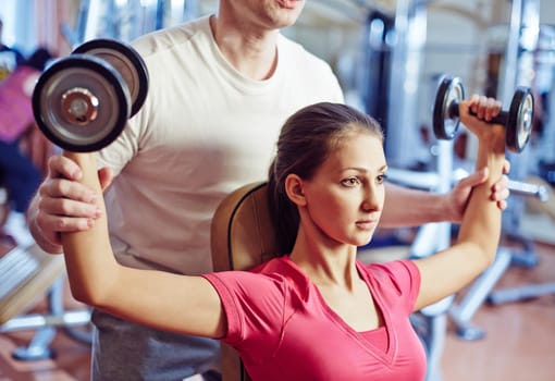 Portrait of pretty girl training in gym with her trainer helping her