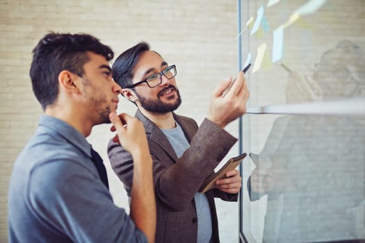 Asian manager pointing at reminder while talking to colleague in office