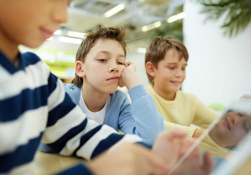 Tired schoolboy looking at digital tablet display with indifferent expression