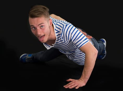 Handsome young man doing single hand push-ups, isolated on black background