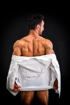 Male bodybuilder undressing revealing muscular back and shoulders, on dark background