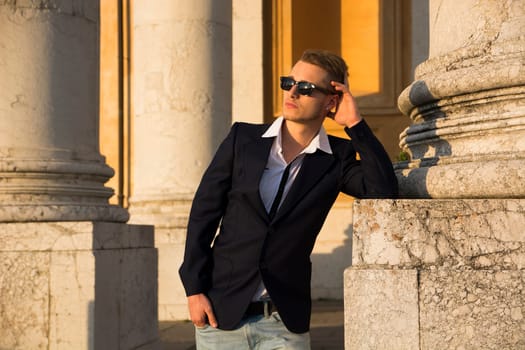 Handsome blond young man with marble columns behind him, looking away