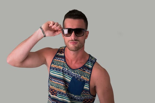 Cool confident young man with sunglasses and tank-top on light grey background
