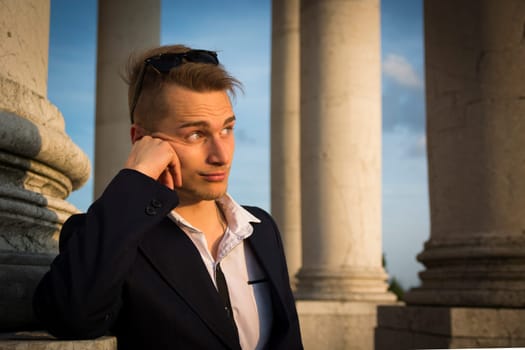 Handsome blond young man with marble columns behind him, looking away
