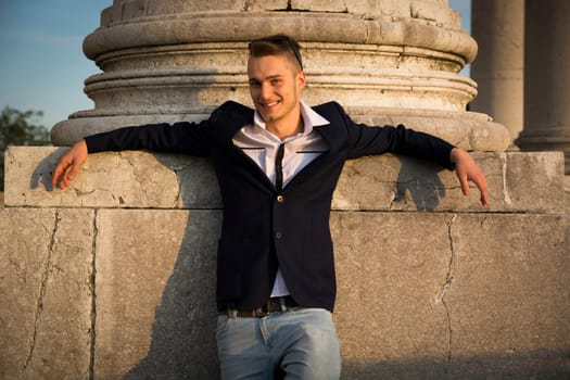Handsome smiling blond young man with marble column behind him, looking at camera