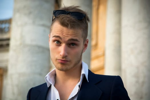 Handsome blond young man with marble columns behind him, looking at camera