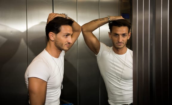 Handsome young man leaning against mirror inside an elevator (lift), looking at camera
