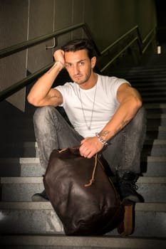 Handsome young man sitting on stairs' granite steps, looking at camera