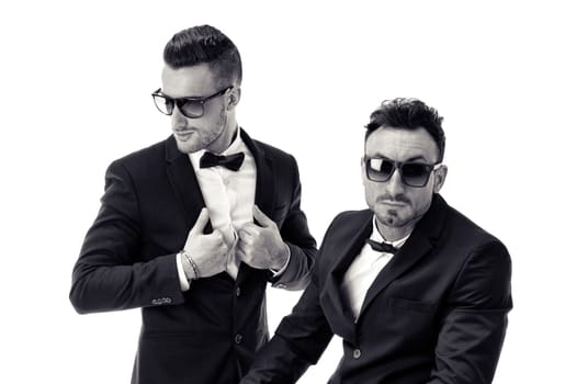 Two elegant men in suit and bowtie isolated on white, one standing, one sitting