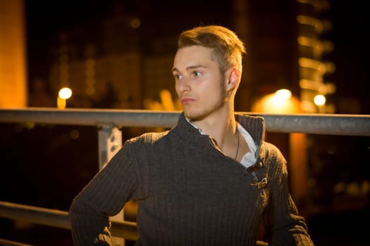 Handsome blond young man alone in urban setting, looking away, night shot