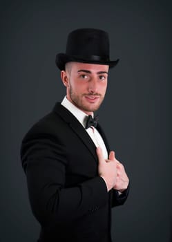 Attractive young businessman with suit, top-hat and bowtie on dark background