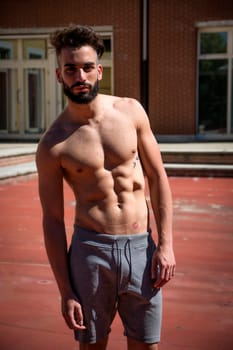 Handsome shirtless young man with beard outdoors, looking at camera