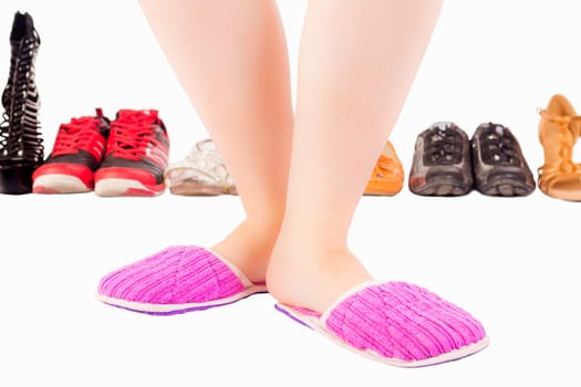 Female legs in pink slippers on white background with different shoes and footwear.
