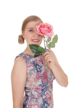 A slim beautiful woman standing in a colorful dress holding.a pink rose over one eye, isolated for white background.