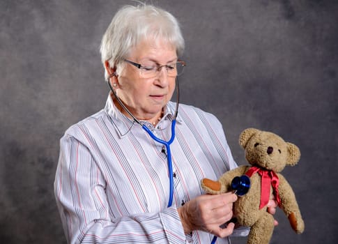 gray haired grandmother with stethoscope is puppet doctor for teddy bear