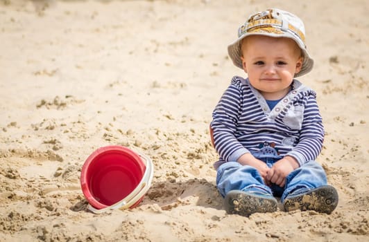 Cute little boy sitting in a sandpit in an outdoor playground