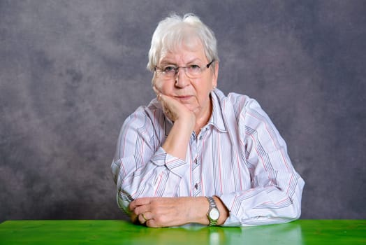gray hairy elderly woman with glasses looking serious in to the camera
