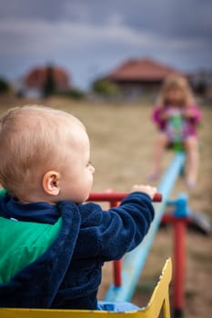 Little boy and his sister having fun on a swing in an outdoor playground