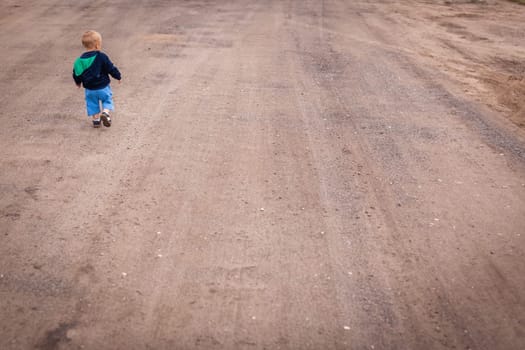 Little boy walking on a gravel, dusty and corrugated village road in the countryside
