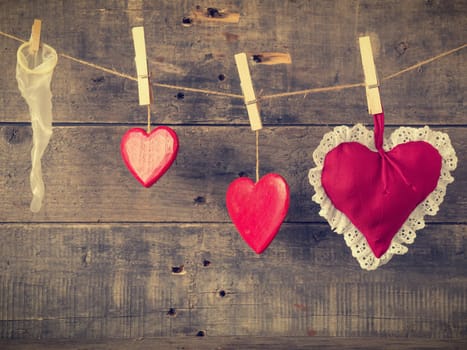 Valentines Day card with red heart shapes and a condome on a wooden wall