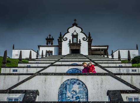 Mother carrying her son while walking up the stairs leading to the entrance of the Our Lady of Peace ( Nossa Senhora da Paz ) chapel above the city of Vila Franca do Campo in Sao Miguel, Azores, Portugal