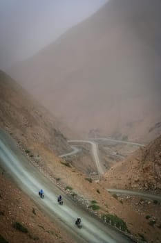 Three cyclists descending on the bicycles on the remote twisting road in Western Tibet