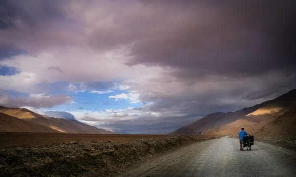 Woman pushing her bicycle uphill on a difficult mountain road on a tibetan plateau, Tibet