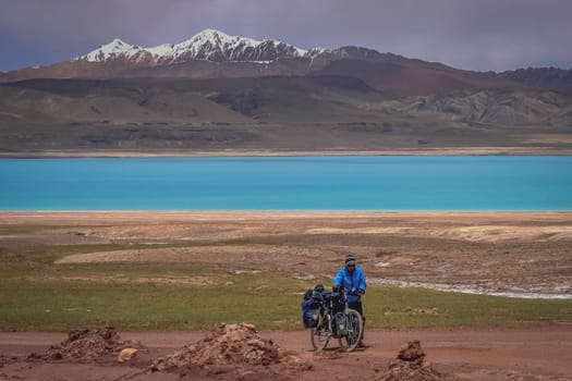Woman pushing her bicycle uphill on a difficult mountain road on a tibetan plateau, Tibet