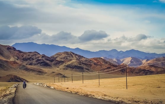 Solo female cyclist on the bicycle on the remote road in Xinjang province leading to Western Tibet
