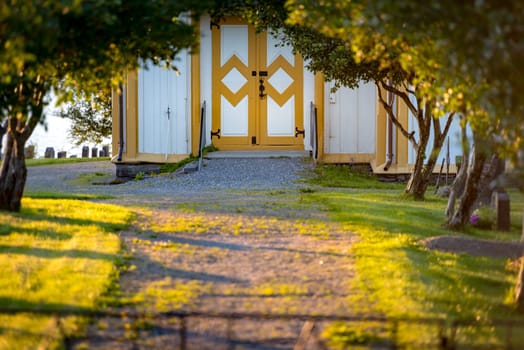 Beautiful nature with green grass and trees. Path to entrance of old house. White wall building with doors. Tranquil view in summer day. Norway, Europe.