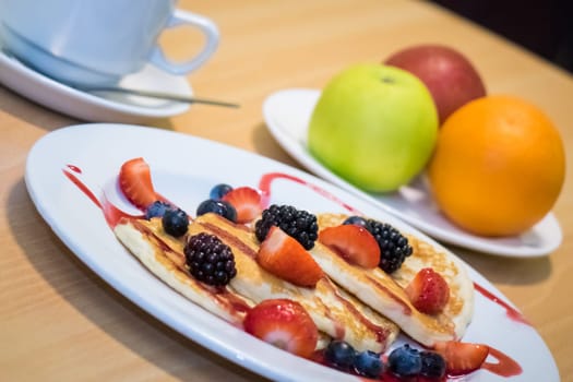 Breakfast meal consisting of pancakes with maple syrup, jam and berries
