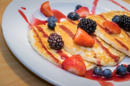 Breakfast meal consisting of pancakes with maple syrup, jam and berries