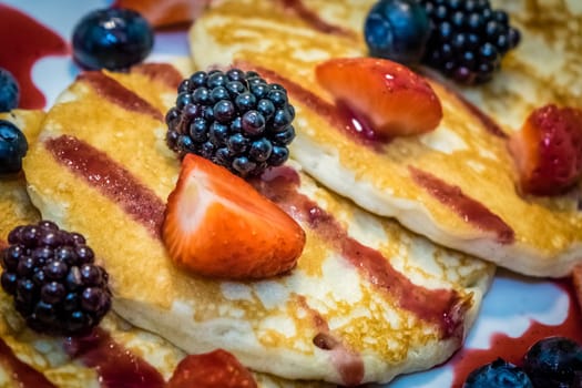 Breakfast meal consisting of pancakes with maple syrup, jam and berries