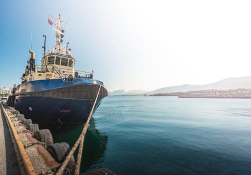 Tugboat or fishing boat in docks of Alesund, Norway, Europe. Ship in foreground and blue sky and mountains in background. Scandinavia travel.