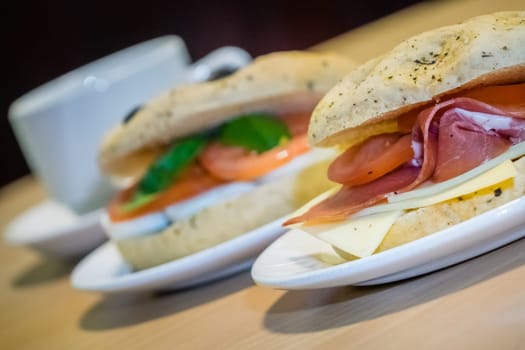 Breakfast bun on a plate, filled with cheddar cheese, prosciutto ham and tomatoes