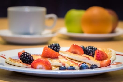 Breakfast meal consisting of pancakes with maple syrup, jam and berries
