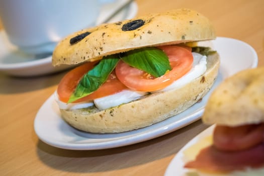 Breakfast bun on a plate, filled with mozzarella, tomato and basil