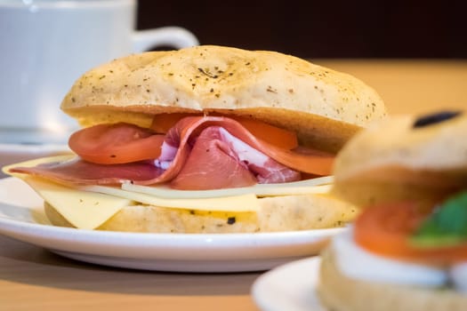 Breakfast bun on a plate, filled with cheddar cheese, prosciutto ham and tomatoes