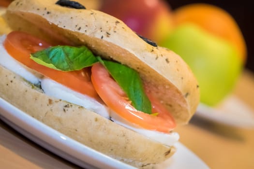 Breakfast bun on a plate, filled with mozzarella, tomato and basil