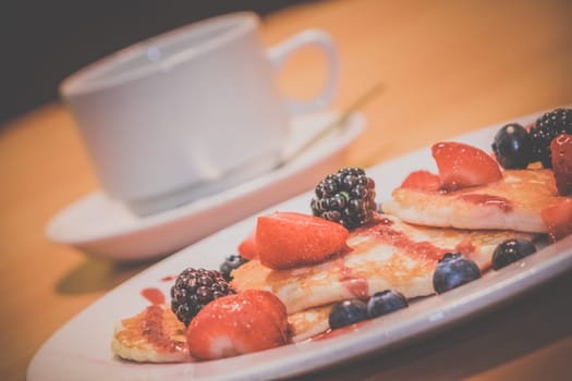 Breakfast meal consisting of pancakes with maple syrup, jam and berries