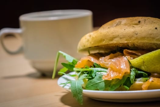Breakfast bun on a plate, filled with smoked salmon and rocket salad